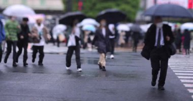 Shibuya 'da yağmurlu bir günde geçitte yürüyen insanların ağır çekimleri.