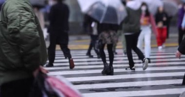 Shibuya 'da yağmurlu bir günde geçitte yürüyen insanların ağır çekimleri.