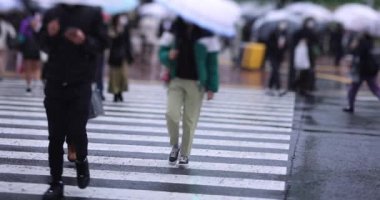 Shibuya 'da yağmurlu bir günde geçitte yürüyen insanların ağır çekimleri.
