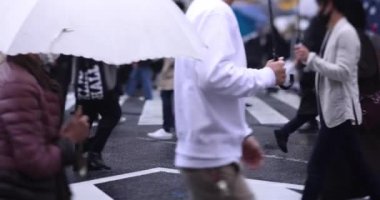 Shibuya 'da yağmurlu bir günde geçitte yürüyen insanların ağır çekimleri.