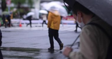 Shibuya 'da yağmurlu bir günde geçitte yürüyen insanların ağır çekimleri.