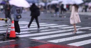 Shibuya 'da yağmurlu bir günde geçitte yürüyen insanların ağır çekimleri.