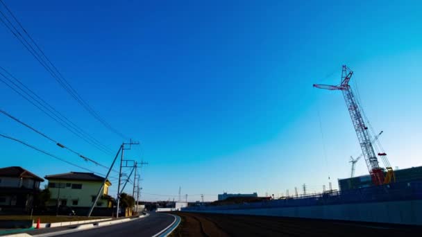 Un lapso de tiempo de grúas en movimiento detrás del cielo azul en el plano ancho en construcción — Vídeos de Stock