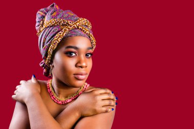 Kırmızı arka planda sarığa sarılı cazibeli koyu tenli kadın.