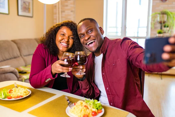 african american couple in love drinking wine from glasses and eating italian pasta in living room 14 february valentines day taking selfie on smartphone camera