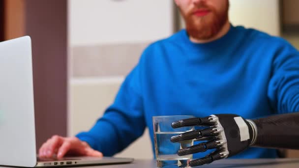 Молодий позаштатний бізнесмен з протезом рука працює вдома в ноутбуці і п'є воду або чай на кухні — стокове відео