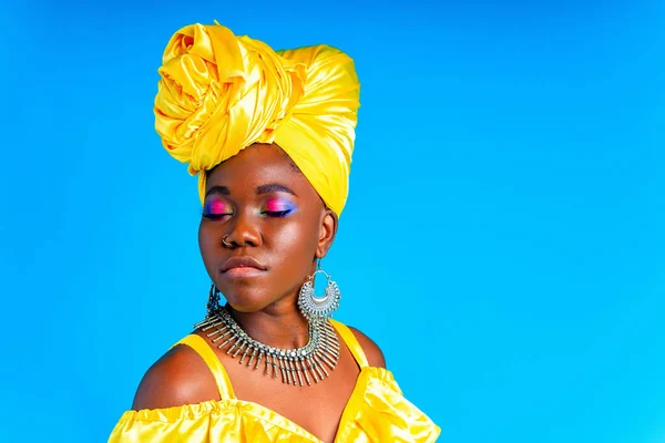 beautiful african woman in yellow silk turban on head and dress with silver neckless and earrings , nose piercing in blue studio background