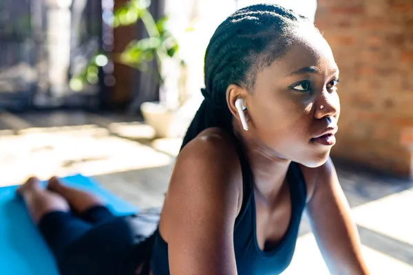 Африканская американка в черном спортивном лифчике делает йогу на полу коврика и слушает аудио медитировать мантру — стоковое фото