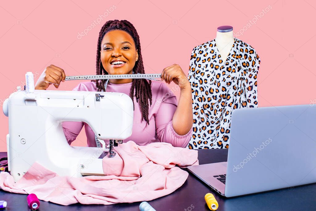 african tailor with afro dreadlocks pigtails sews clothes on sewing machine at tailor office pink wall background