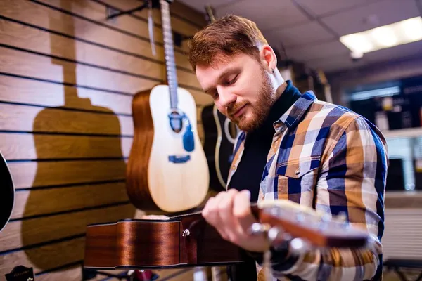 Kızıl saçlı kızıl adam gitar dükkanından kaliteli akustik gitar seçiyor.