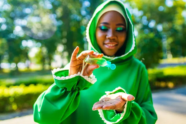 Muslimische Frau in grünem Hijab und Nasenpiercing trägt im Freien im Sommerpark ein antiseptisches Gel auf — Stockfoto