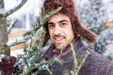 Yakışıklı Rus adam dışarıda noel ağacı alışverişi yapıyor.