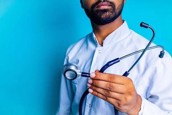Pakistański lekarz w białym płaszczu ze stetoskopem na tle niebieskiego studia — Zdjęcie stockowe