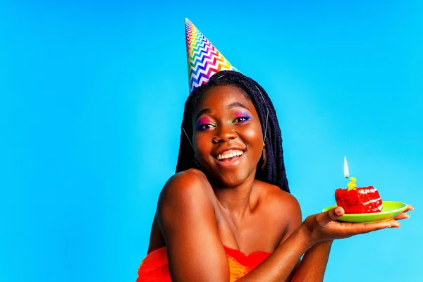 Schöne Afro-Frau mit georgischem Make-up tragen Geburtstagsmütze und halten Kuchen im blauen Studio — Stockfoto