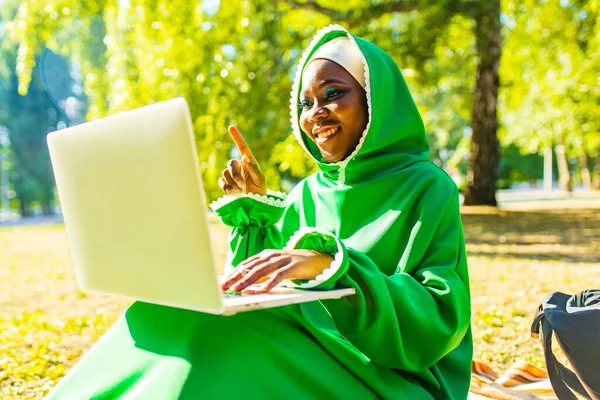 Mladá krásná muslimská obchodní žena s moderním make-up nosit zelené hidžáb a používání notebooku, zatímco sedí v letním parku — Stock fotografie