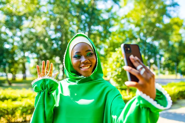 Латиноамериканская арабская женщина в зеленом мусульманском платье с современным ярким макияжем и пирсингом носа делает селфи на улице — стоковое фото