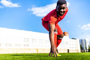 Mutlu çok kültürlü İspanyol futbolcu gülümsüyor ve açık hava güneşli bir günde kırmızı spor takım elbise giyiyor.