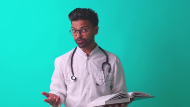 Indyjski brodaty kardiolog człowiek w okularach oczy w białym płaszczu medycznym ze stetoskopem w tle niebieskie studio przekazując dobrą wiadomość — Wideo stockowe