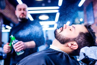 Arap yakışıklı sakallı adam berber dükkanında saçını kestiriyor.