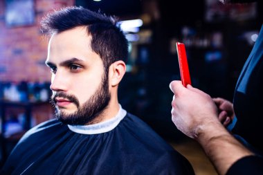 Arap yakışıklı sakallı adam berber dükkanında saçını kestiriyor.