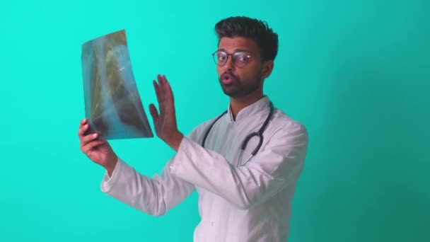 Indyjski lekarz pokazując klatki piersiowej kości film rentgenowski obraz w niebieskim studio baclground — Wideo stockowe