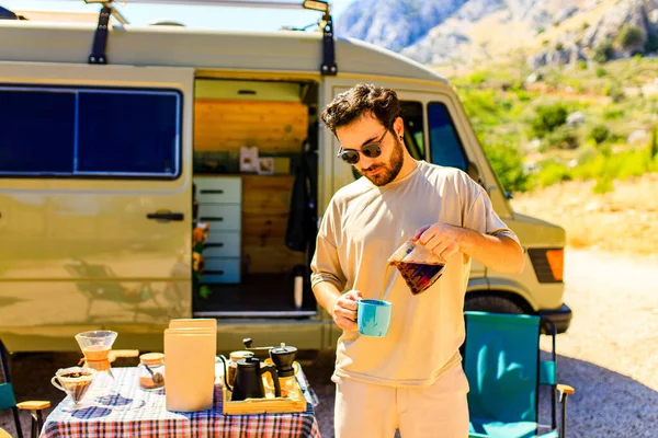 Homem em charmosa casa de reboque faz café ao ar livre em montanhas no verão dia ensolarado — Fotografia de Stock