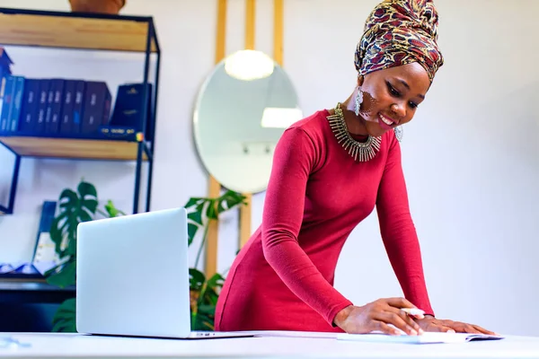 Изображение африканской американки с тюрбаном над головой, использующей ноутбук в офисе — стоковое фото
