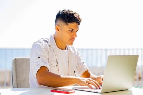 Freiberuflicher junger Mann in weißem Hemd arbeitet mit Laptop im Strandcafé — Stockfoto