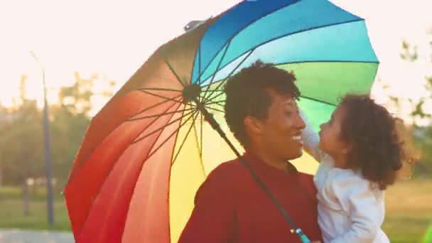 Blandras familj som täcker från solen under det ljusa paraplyet — Stockvideo