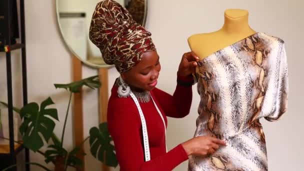 Tanzanian mujer con serpiente impresión turbante sobre escuchar a trabajar en dressmaking tienda — Vídeos de Stock