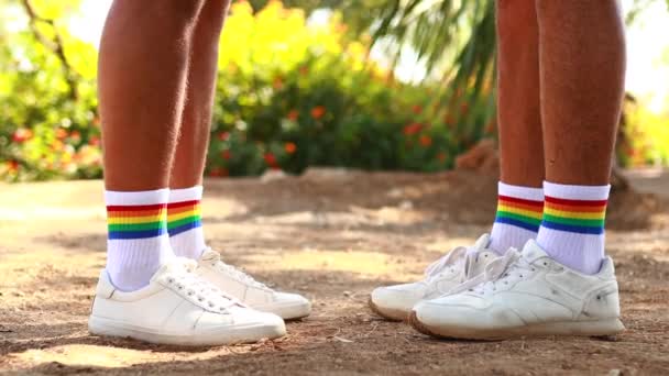 Primer plano de zapatos con arcoíris calcetines blancos de dos hombres jóvenes mientras se besan al aire libre — Vídeos de Stock