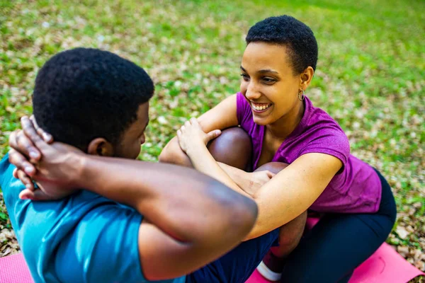 Fuerte y poderosa pareja afroamericana enamorada están haciendo ejercicios abdominales al aire libre en el parque o el bosque — Foto de Stock