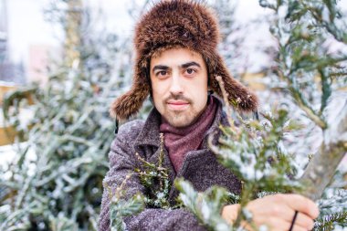 Şık yün ceketli Hintli bir adam dışarıda kar altında bir Noel ağacı satın alıyor.