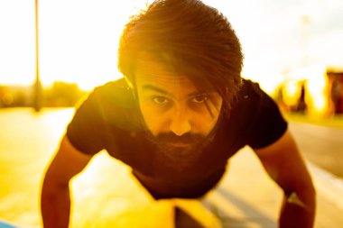 Siyah pamuklu tişörtlü sakallı adam güneş ışığı altında yaz parkında ısınıyor.