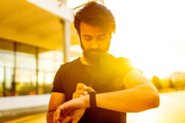 Siyah pamuklu tişörtlü sakallı adam güneş ışığı altında yaz parkında ısınıyor.