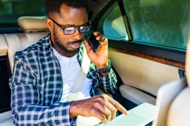 Afrikalı Amerikalı iş adamı bir arabanın koltuğunda otururken telefonla konuşuyor.