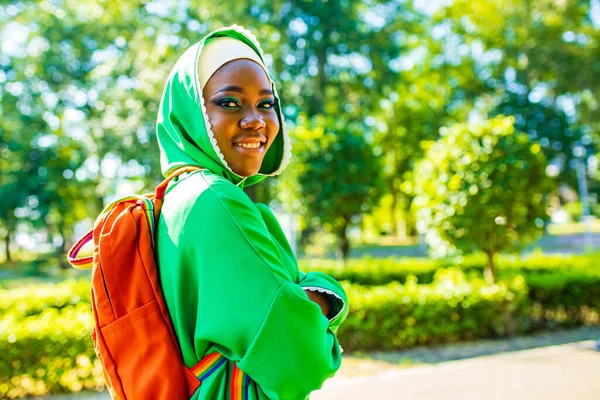 Африканська жінка в зеленому хіджабі з яскравим макіяжем з райдужним рюкзаком в літньому парку — стокове фото
