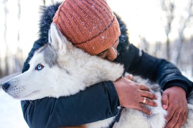 Karışık ırk adamı kış parkında köpeğine sarılıyor.