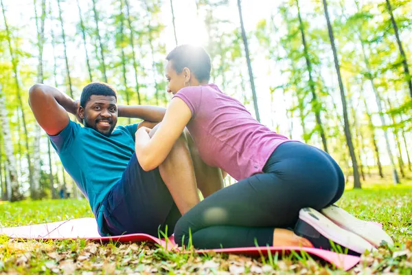 Fuerte y poderosa pareja afroamericana enamorada están haciendo ejercicios abdominales al aire libre en el parque o el bosque — Foto de Stock