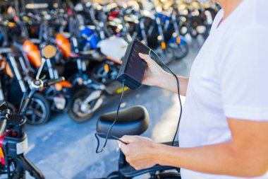 Erkek ellerinin elektrikli scooterın pilini şarj ederken çekilmiş bir fotoğrafı.