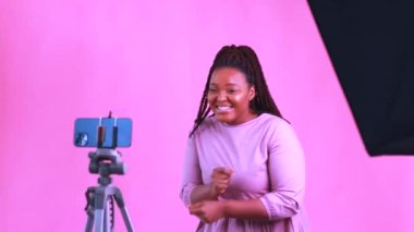 Saçları örgülü, sarı saçlı İspanyol kadın stüdyoda aboneleriyle telefonda konuşurken pembe elbise giyiyor.