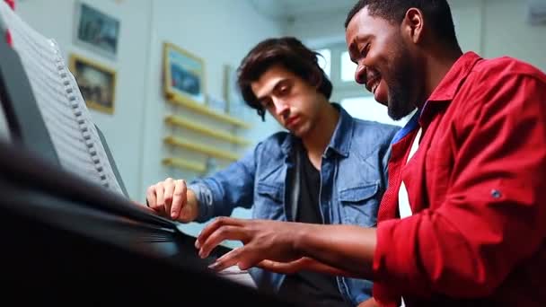 Латинський іспаномовний чоловік вчиться грати на піаніно з кавказьким вчителем у класі — стокове відео