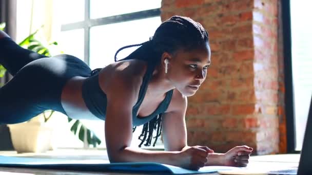 Mezcla de raza nigeriana mirando a la pantalla del ordenador portátil haciendo mientras está acostado en la esterilla de yoga en el suelo — Vídeos de Stock