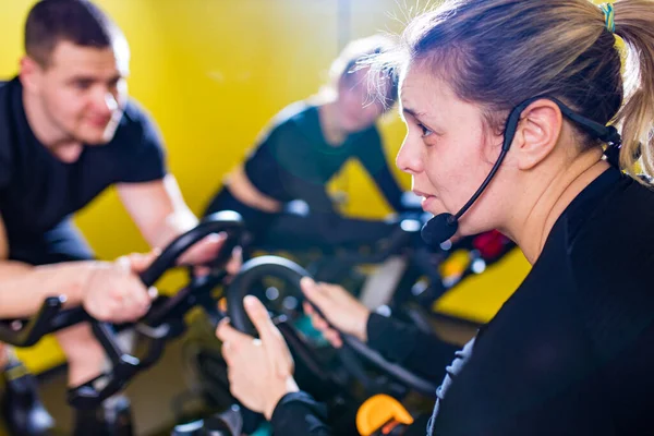 Abbastanza autentico istruttrice con auricolare in esercizio di classe di fitness con gruppo in sala ciclismo — Foto Stock
