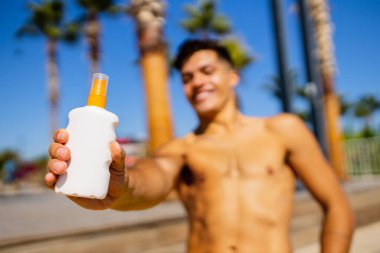 Güneşli bir günde plajda köpük kremi kullanan iri yarı, Brezilyalı bir adam.