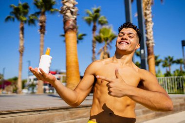 Güneşli bir günde plajda köpük kremi kullanan iri yarı, Brezilyalı bir adam.