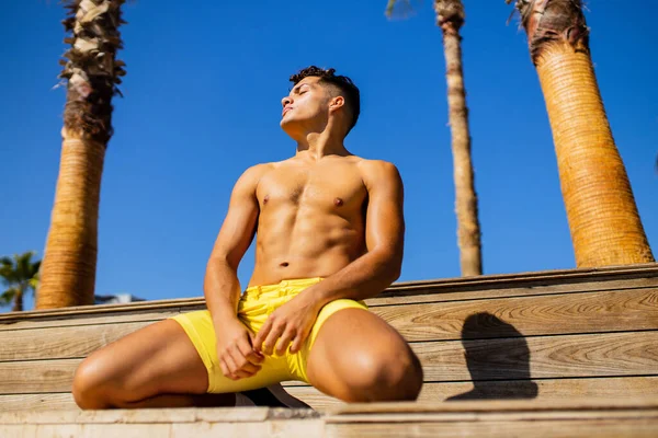 Homem latino aplicando loção bronzeado do sol no mar com palmas de fundo — Fotografia de Stock