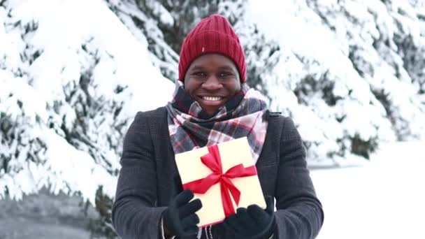 Spanish man give a beautuful giftbox with red ribbon outdoor in winter park — Stock video