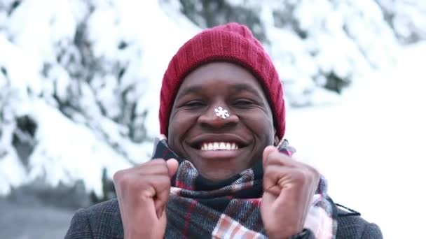 Збуджений іспаномовний чоловік у червоній шапці зі сніжинкою на обличчі розважається і відчуває різдвяний настрій у парку — стокове відео