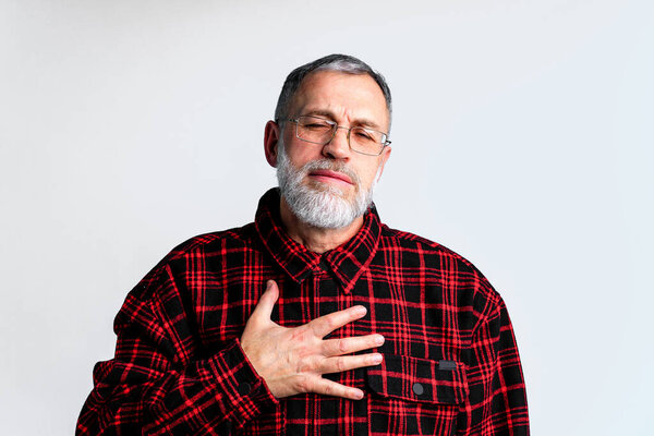 Portrait of mature man isolated on grey background suffering from severe heart ache, closing eyes to relieve pain